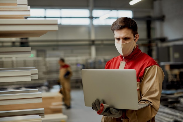 Travailleur manuel travaillant sur un ordinateur portable dans un entrepôt de menuiserie pendant la pandémie de coronavirus