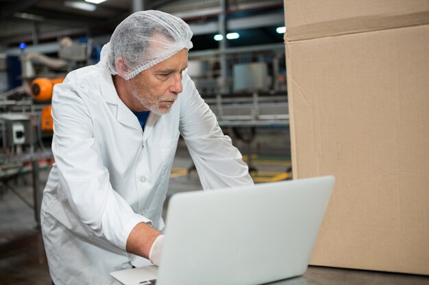 Travailleur masculin à l'aide d'un ordinateur portable dans une usine de boissons froides