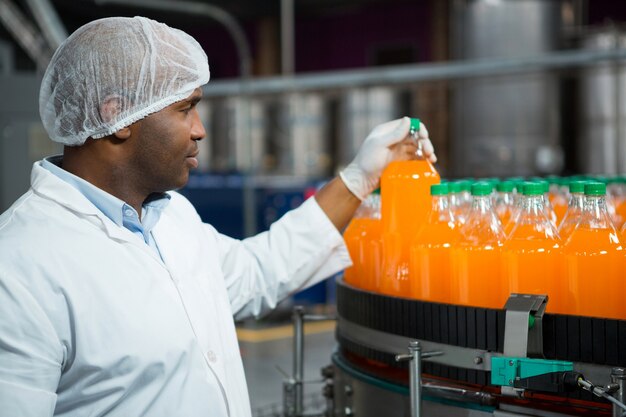 Travailleur masculin contrôle des bouteilles de jus en usine