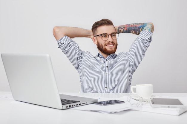 Travailleur masculin créatif détendu et insouciant se pose alors qu'il est assis au bureau regarde pensivement de côté