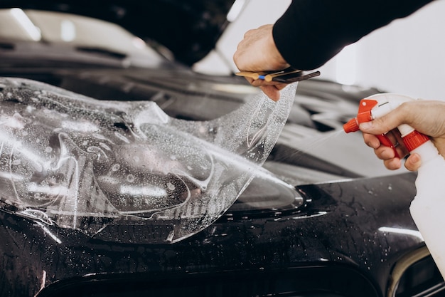 Travailleur masculin enveloppant une voiture avec une feuille de protection