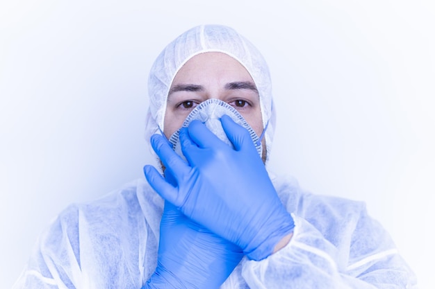 Travailleur médical dans une combinaison en plastique mettant un masque facial avec des gants en plastique bleus