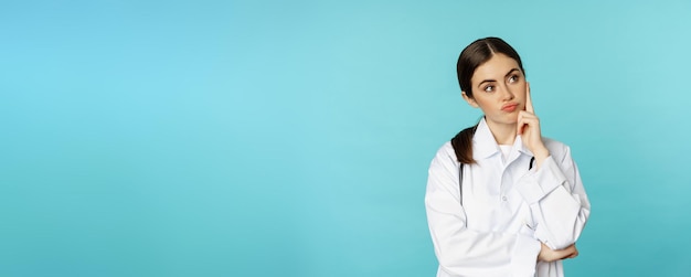 Travailleur médical réfléchie jeune femme médecin à la recherche d'ennui sans amusement debout en blouse blanche contre b