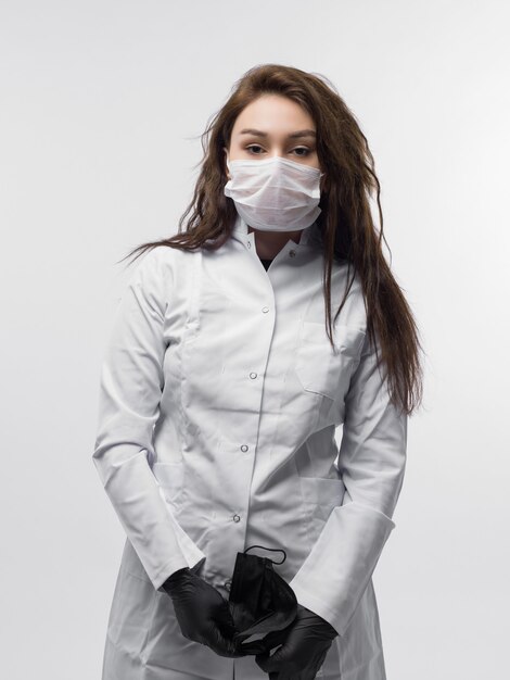 Travailleur médical en uniforme de médecin blanc avec masque de protection tenant un masque noir dans ses mains