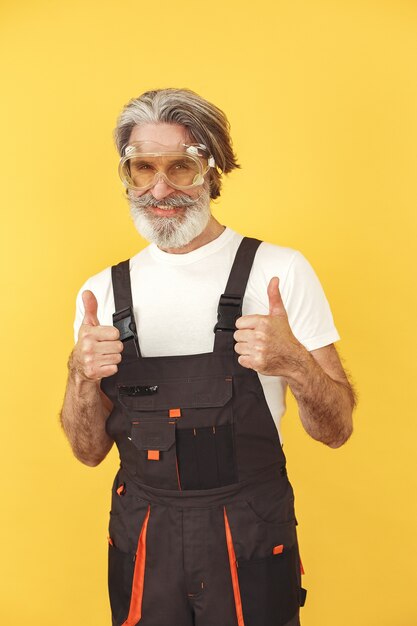 Travailleur en salopette. Homme avec des outils. Senior à lunettes jaunes.