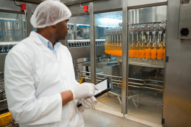 Travailleur de sexe masculin inspectant les bouteilles de jus en usine