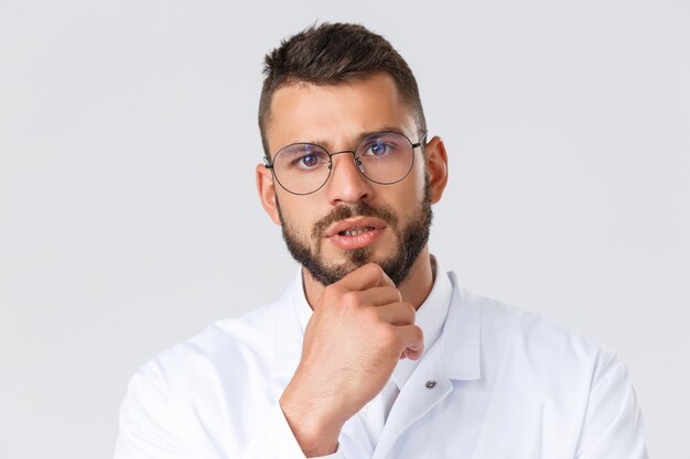 Travailleurs de la santé, coronavirus, concept de pandémie de covid-19. Gros plan sur un médecin professionnel à l'air sérieux en lunettes et blouse blanche, toucher le menton réfléchi, penser, prendre une décision sur le patient