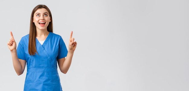 Les travailleurs de la santé préviennent le concept de médecine de dépistage des tests de covid19 du virus Enthousiaste souriante jolie femme médecin ou infirmière en gommages bleus pointant les doigts vers le haut et levant les yeux en se réjouissant