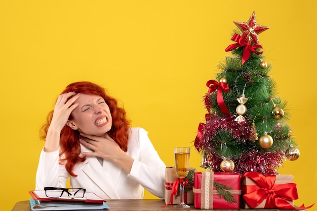 Travailleuse assise derrière la table avec des cadeaux de Noël et arbre sur jaune