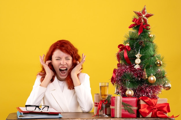 Travailleuse assise derrière la table avec des cadeaux de Noël et arbre sur jaune