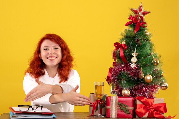 Travailleuse assise derrière la table avec des cadeaux de Noël et arbre sur sol jaune bureau couleur nouvel an