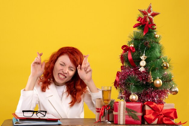 Travailleuse assise derrière la table avec des cadeaux de Noël et des arbres en espérant sur jaune