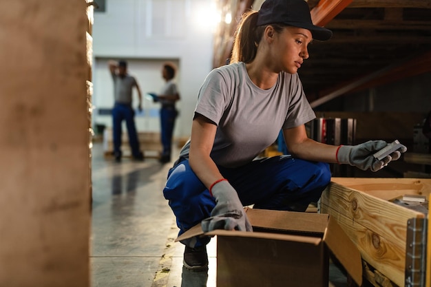 Travailleuse préparant l'expédition et emballant les produits manufacturés dans une boîte en carton dans un entrepôt de distribution