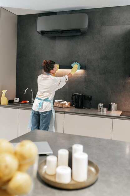 Travaux ménagers. Jeune femme brune nettoyant la lampe dans la cuisine