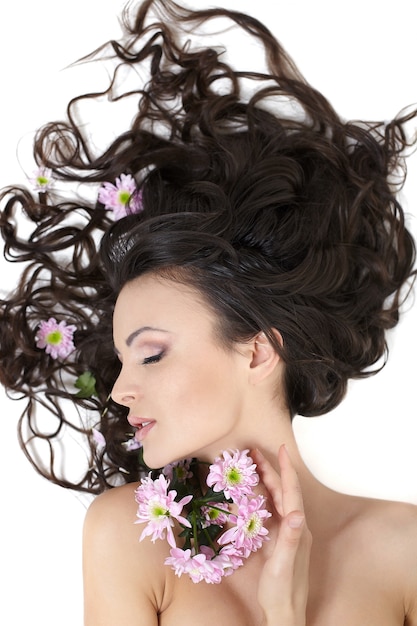 Très belle fille allongée avec des fleurs aux cheveux brillants dans ses cheveux maquillage lumineux isolé sur blanc
