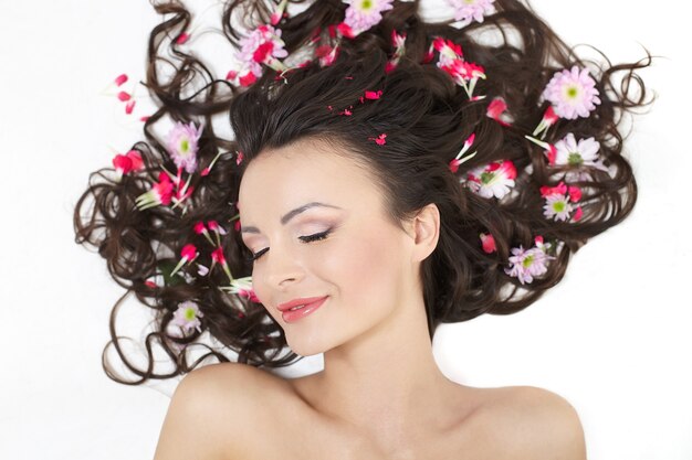 Très belle fille allongée avec des fleurs rouges vives dans ses cheveux maquillage lumineux isolé sur blanc