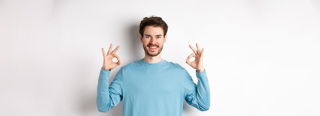 Photo gratuite très bon beau mec souriant montrant des signes corrects et ayant l'air satisfait debout sur fond blanc