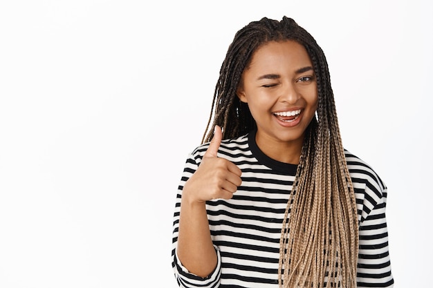 Très bon clin d'œil de fille noire de soutien souriant montrer le pouce vers le haut dans l'approbation comme et recommander le produit ou l'entreprise fond blanc