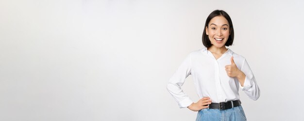 Très bonne femme entrepreneure asiatique enthousiaste et souriante montrant le pouce vers le haut en éloge d'approbation excellent travail satisfait des résultats debout sur fond blanc