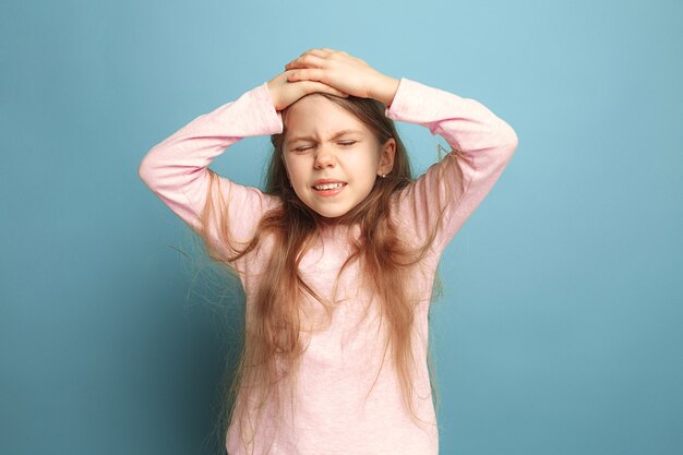 triste adolescente avec maux de tête ou douleur sur fond bleu studio. Concept d'expressions faciales et d'émotions de personnes.