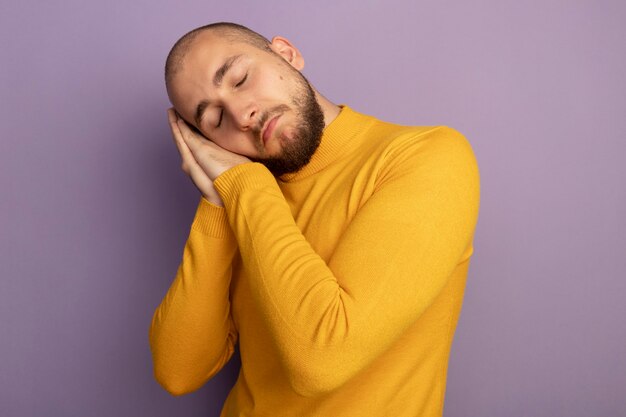 Triste aux yeux fermés jeune beau mec montrant le geste de sommeil isolé sur un mur violet