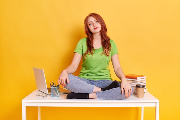 Triste femme ennuyée utilisant un ordinateur portable assis assis sur une table avec les jambes croisées