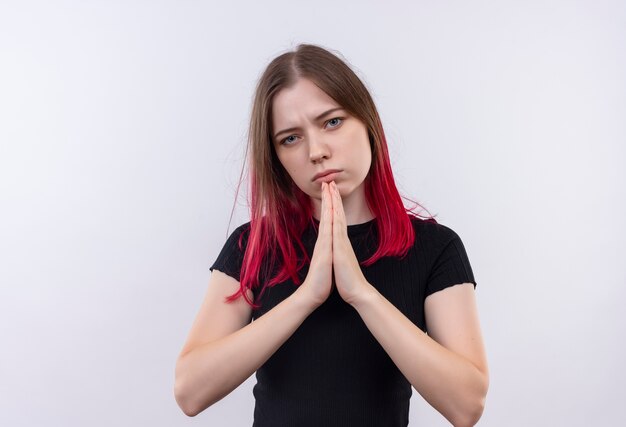 Triste jeune belle fille portant un t-shirt noir montrant le geste de prier sur fond blanc isolé