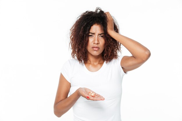 Triste jeune femme africaine tenant des pilules avec maux de tête.