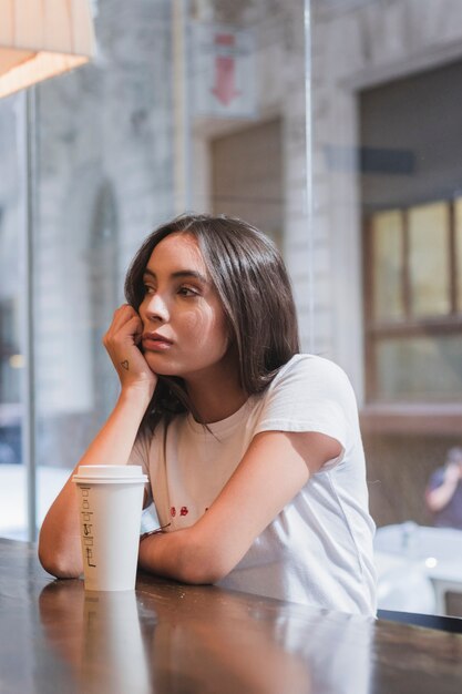 Triste jeune femme assise au café avec une tasse de café à emporter sur une table en bois