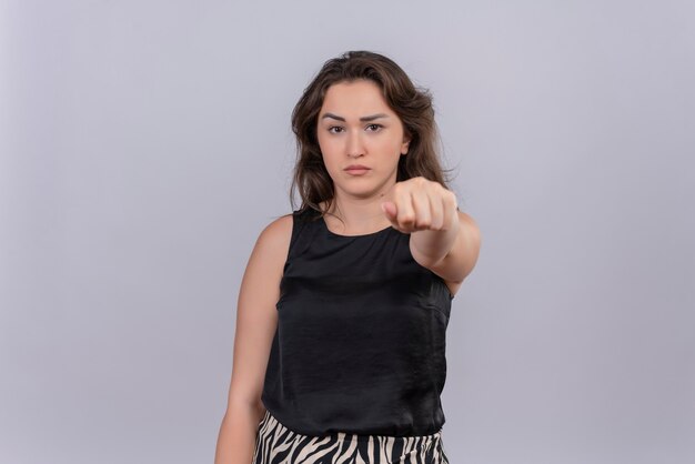 Triste jeune femme portant un maillot de corps noir a tendu le poing pour avancer sur le mur blanc