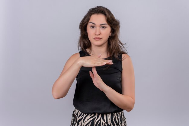 Triste jeune femme portant un maillot noir montre le geste de délai d'attente sur le mur blanc