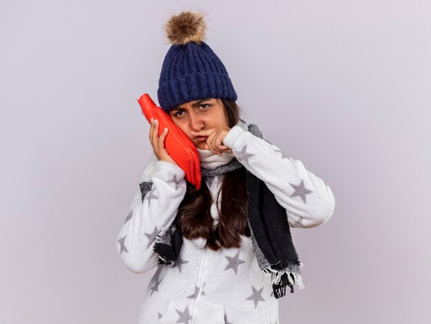 Triste jeune fille malade à côté portant un chapeau d'hiver avec écharpe mettant le sac d'eau chaude sur la joue