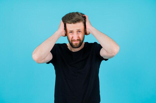 Triste jeune homme met les mains sur la tête sur fond bleu