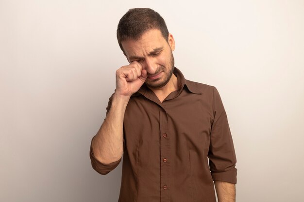 Triste jeune homme de race blanche essuyant les yeux avec les yeux fermés isolé sur fond blanc avec copie espace