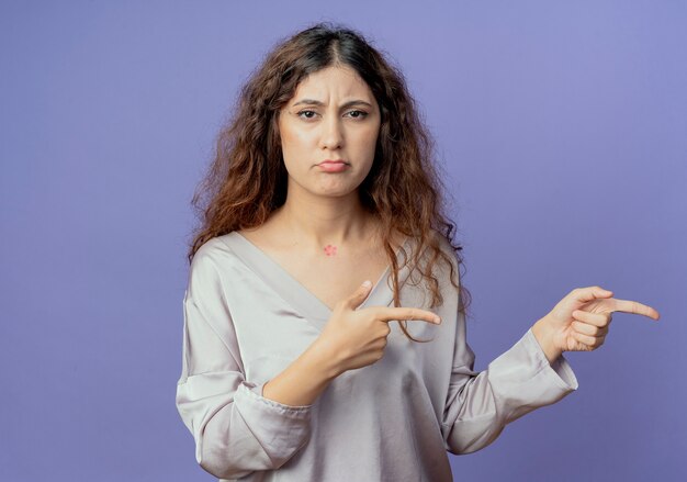 Triste jeune jolie fille pointe sur le côté isolé sur un mur bleu avec espace de copie