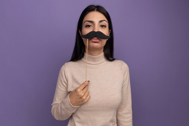 Triste jolie fille de race blanche brune tient une fausse moustache sur bâton violet