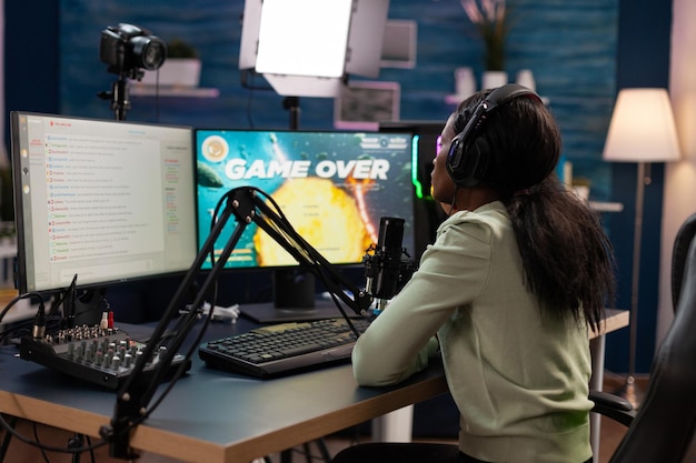 Triste joueur professionnel nerveux assis au bureau de jeu jouant à des jeux vidéo de tir spatial perdant le championnat de jeux en ligne. Femme esport bouleversée diffusant en direct à l'aide d'un équipement informatique RVB, jeu terminé à l'écran