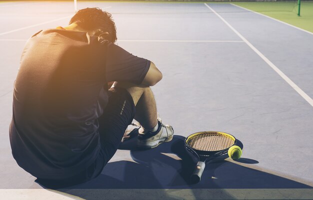 Triste joueuse de tennis assise sur le court après avoir perdu un match