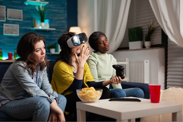 Tristes amies nerveuses assises sur couh jouant à des jeux vidéo en ligne à l'aide d'un casque et d'un joystick vr