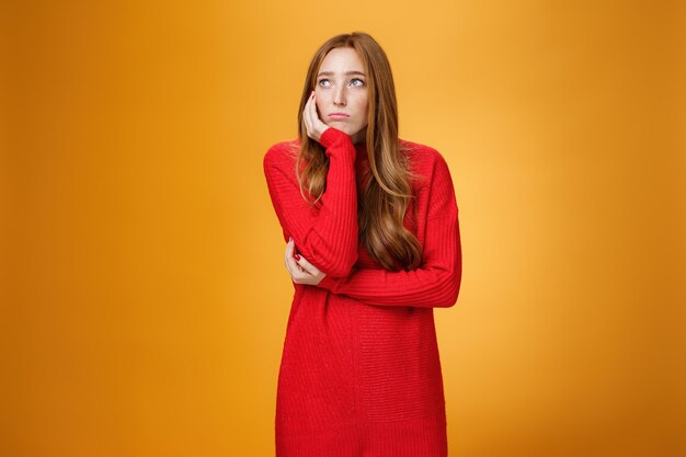 Tristesse et contrariété femme solitaire penchée la tête sur la paume dans une pose contrariée, l'air sombre dans le coin supérieur gauche comme se souvenant d'une histoire malheureuse ou s'ennuyant debout mal à l'aise sur le mur orange