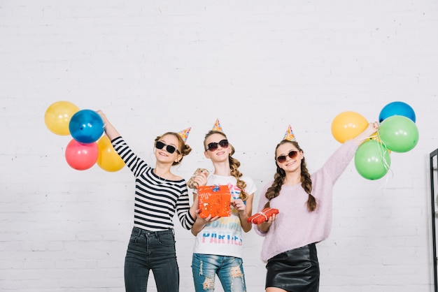 Trois amies adolescentes tenant des boîtes-cadeaux emballés, debout contre le mur