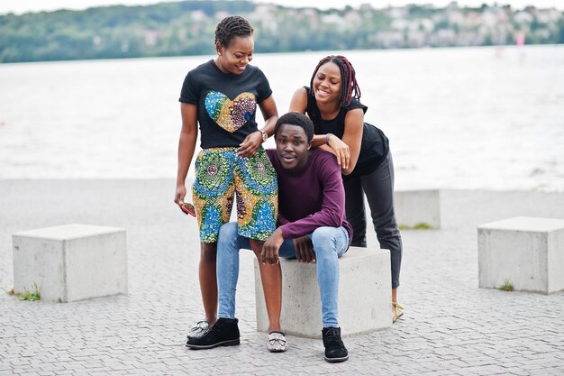 Photo gratuite trois amis afro-américains assis sur des cubes de pierre en plein air