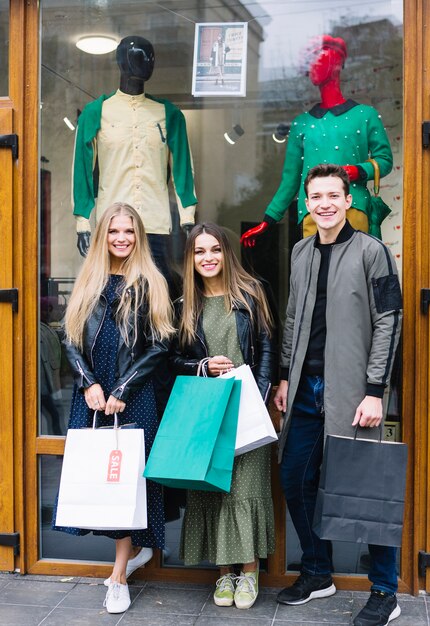 Trois amis élégants, debout devant une vitrine tenant des sacs à provisions