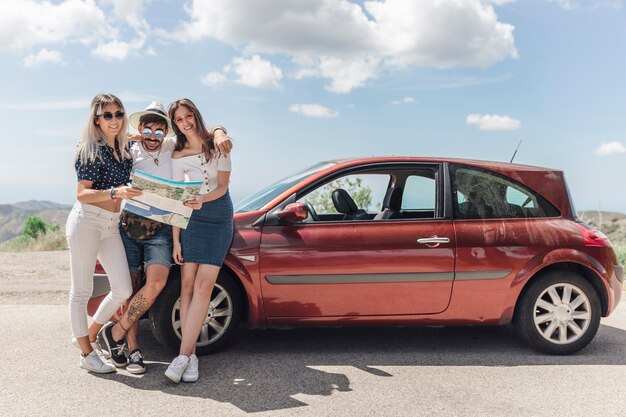 Trois amis tenant la carte debout près de la voiture moderne sur route