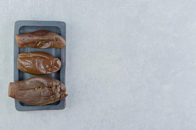 Trois aubergines marinées sur le plateau, sur la surface en marbre