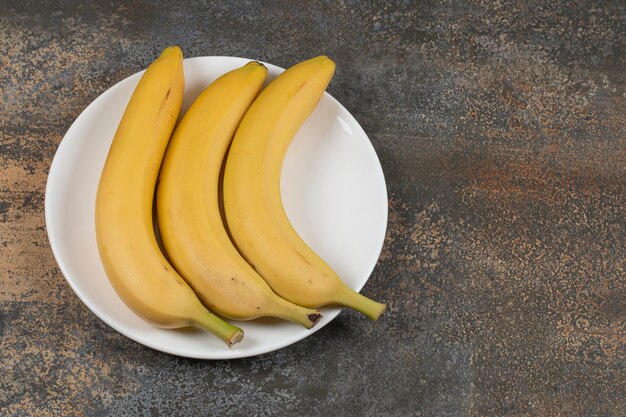 Trois bananes mûres sur plaque blanche.