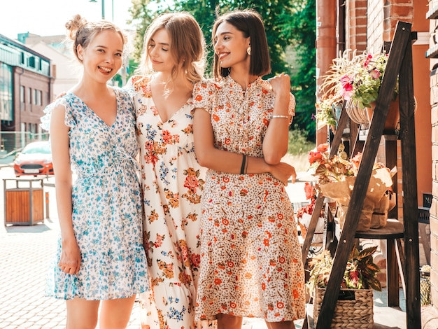 Trois belles filles souriantes en robe d'été à la mode posant dans la rue