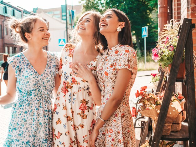 Trois belles filles souriantes en robe d'été à la mode posant dans la rue