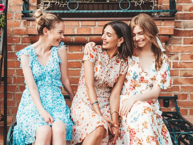 Trois belles filles souriantes en robe d'été à la mode posant dans la rue