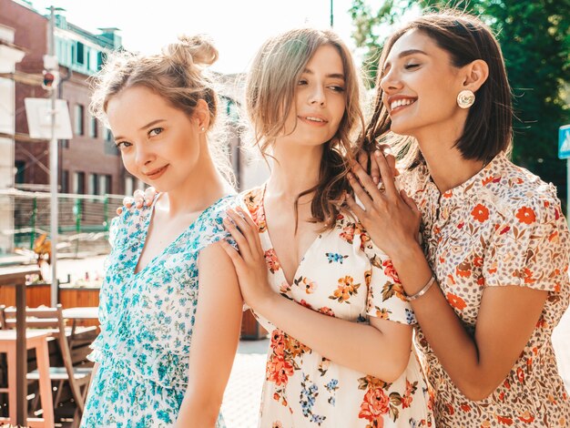 Trois belles filles souriantes en robe d'été à la mode posant dans la rue